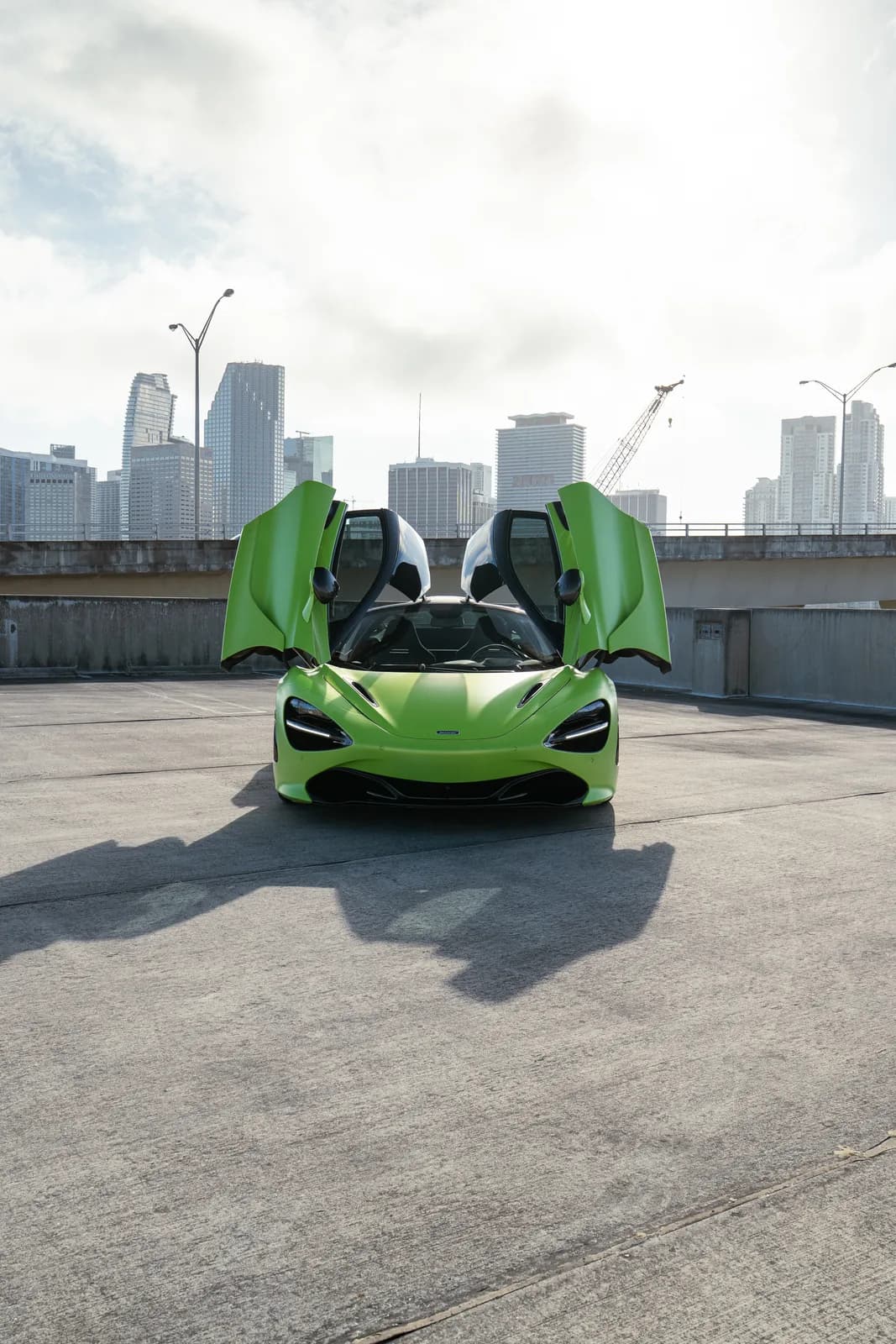 Green McLaren 720S with doors up, downtown Miami behind